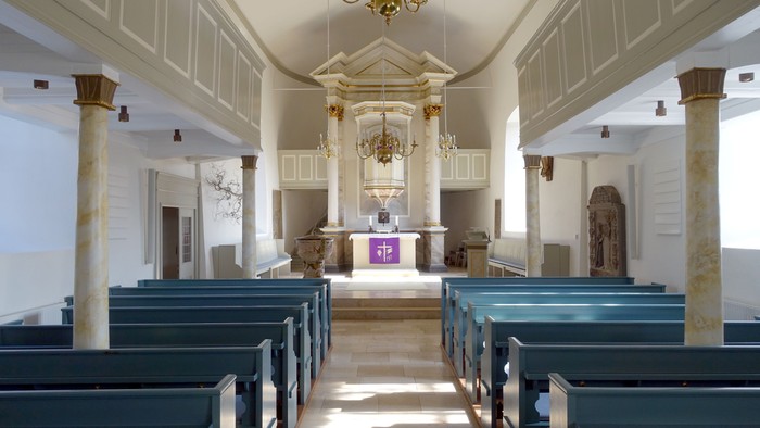 Die Kirche hat blaue Bänke und weiße Säulen.