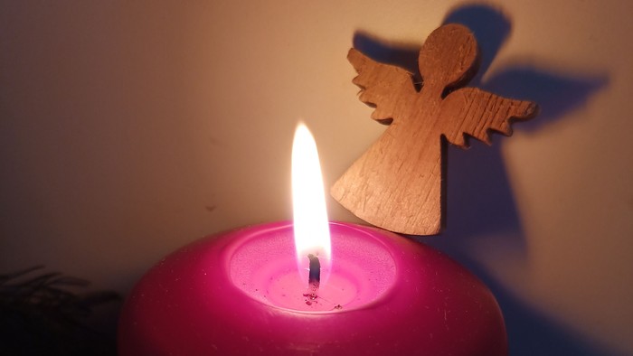 Eine brennende rote Kerze mit einem Holzengel darauf.