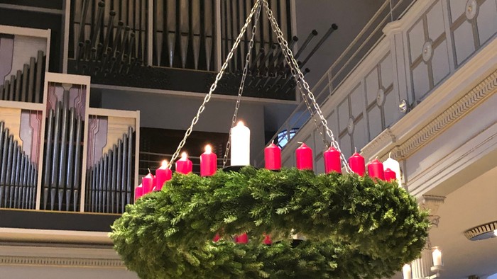 Ein großer Weihnachtskranz mit roten Schleifen hängt von der Decke in einem großen Raum mit Orgel.