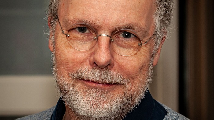 En mand med briller og skæg iført en grå sweater med en mørk krave.