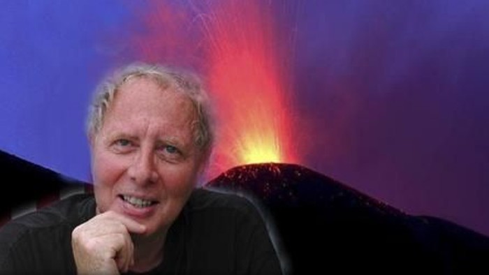 En person poser gladt foran et dramatisk vulkanudbrud med glødende lava og røg.