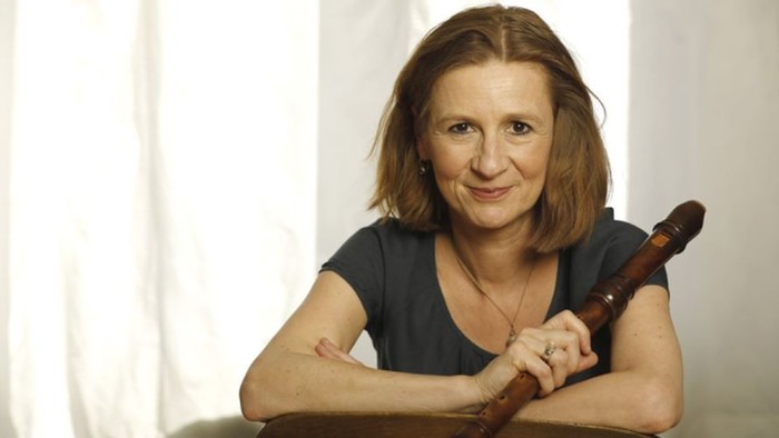 Eine Frau, die lächelnd ein hölzernes Blockflöteninstrument hält.