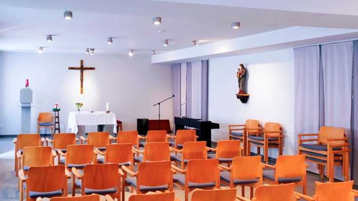 Kirchliche Kapelle mit orangefarbenen Stühlen und Kreuz
