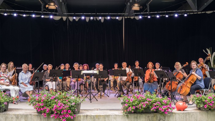 Das Orchester spielt auf der Bühne, umgeben von lebendigen Blumenarrangements, während ein Dirigent das Ensemble leitet.