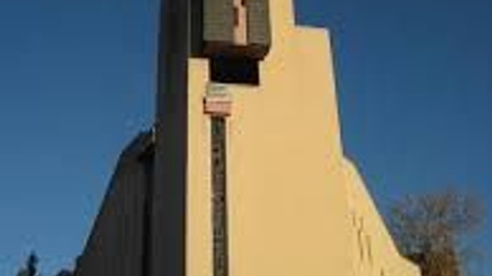 Das Bild zeigt eine moderne Kirche mit einem großen Kreuz vor einem klaren blauen Himmel.