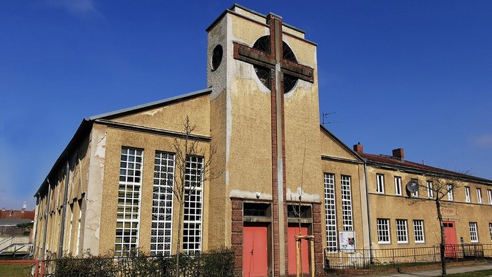 Gelbe Kirche mit hohem Turm und roter Tür unter blauem Himmel