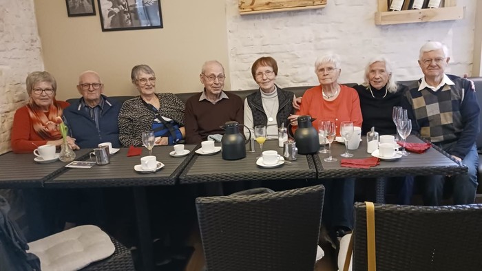 Eine Gruppe älterer Menschen sitzt bei Tee und Kaffee an einem Tisch.