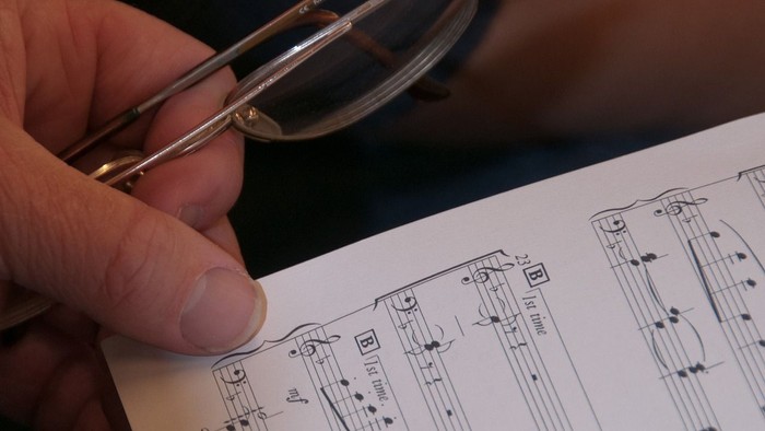 Hand hält Brille über aufgeschlagenem Buch mit Notenblatt