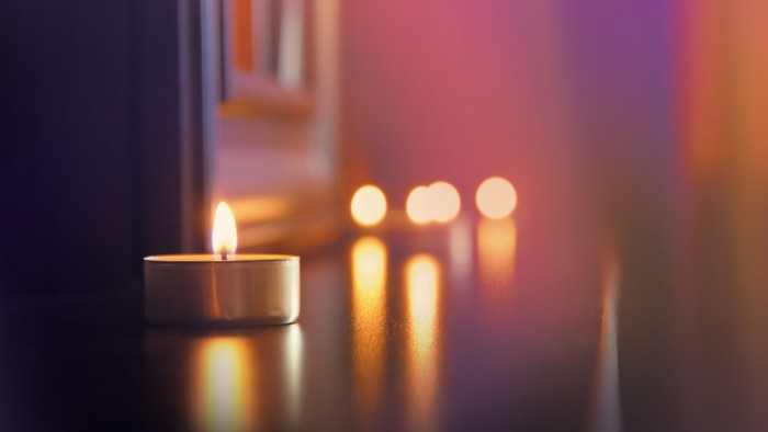 Ein brennendes Teelicht im Vordergrund, mehrere unscharfe Kerzen im Hintergrund
