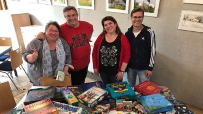 Vier Personen stehen hinter einem Tisch mit vielen Büchern und Spielen.