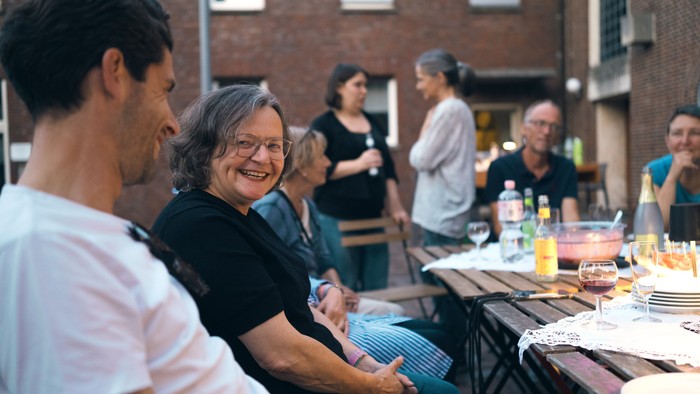 Eine Gruppe von Menschen versammelte sich im Freien um einen Tisch, lächelte und unterhielt sich.