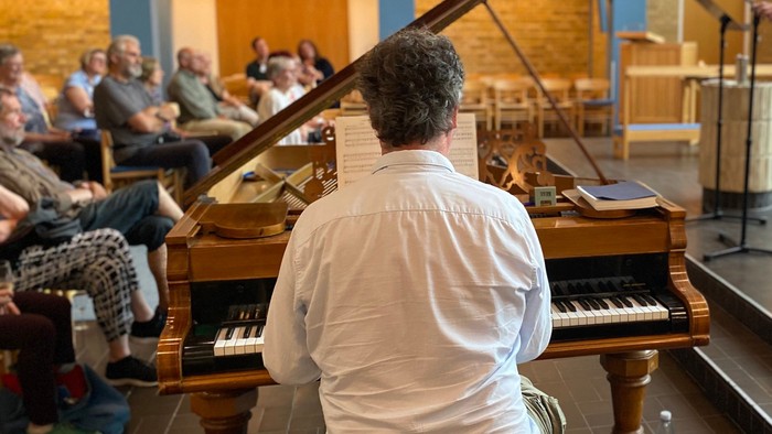 Musikere, der optræder i en rummelig sal med et publikum, der sidder og lytter opmærksomt.