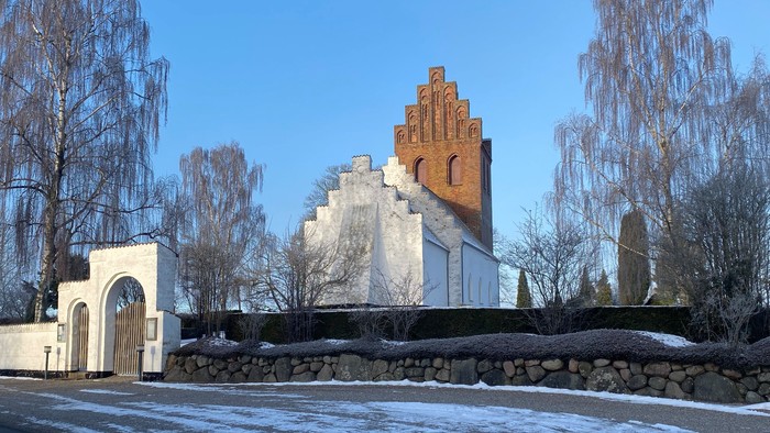 En lille kirke med tårn og mursten i en snedækked landsby.