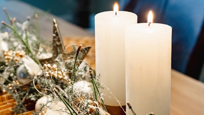 Zwei weiße brennende Kerze an an einem Advents-Gesteck.
