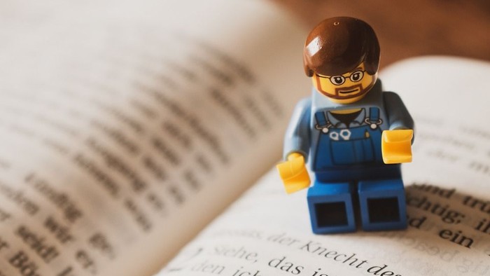 Ein Lego-Männchen sitzt auf einem aufgeschlagenen Buch.