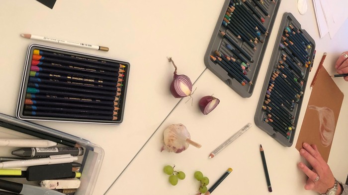 En person sidder ved et bord med blyanter, frugter og notatblokke.