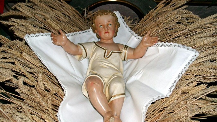 Puppe in weißem Stoff, umgeben von Stroh.