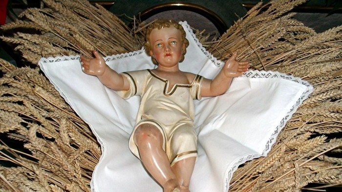 Puppe in weißem Stoff, umgeben von Stroh.