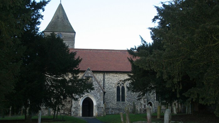 Church with red roof and tall steeple, surrounded by trees and gravestones.
