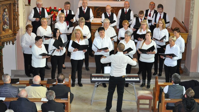 Ein Chor singt in einer Kirche, dirigiert von einem Mann am Klavier