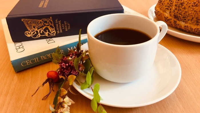 En kop kaffe, en bog og en kage på bordet