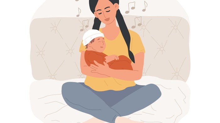 Eine Frau hält ein Baby im Arm und sitzt auf einem Bett.