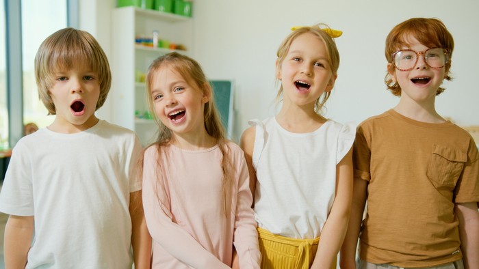 Vier fröhliche Kinder, die lachend und freudig zusammen drinnen posieren.