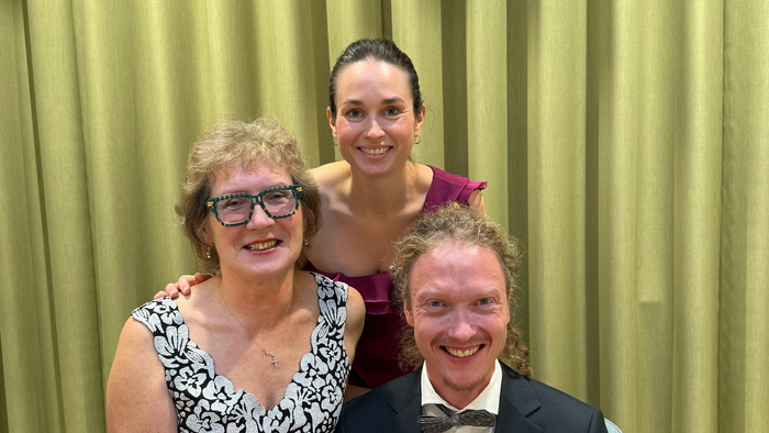 Tre glade mennesker, der poser sammen i formelt tøj til en begivenhed og smiler varmt.