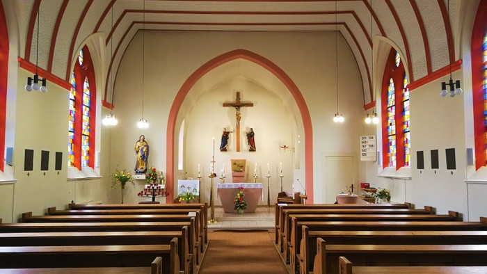 Innenraum einer Kirche mit Holzbanken und hohem Gewoelbe.