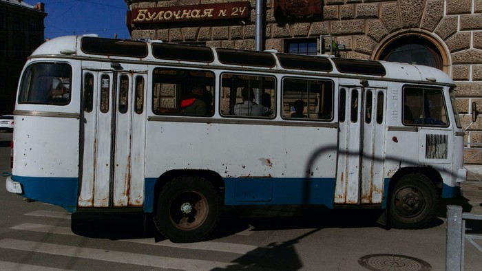 En gammel, rusten bus står foran et stenhus.