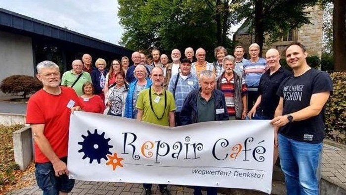 Gruppe von Menschen, die ein „Repair-Café“-Banner halten.