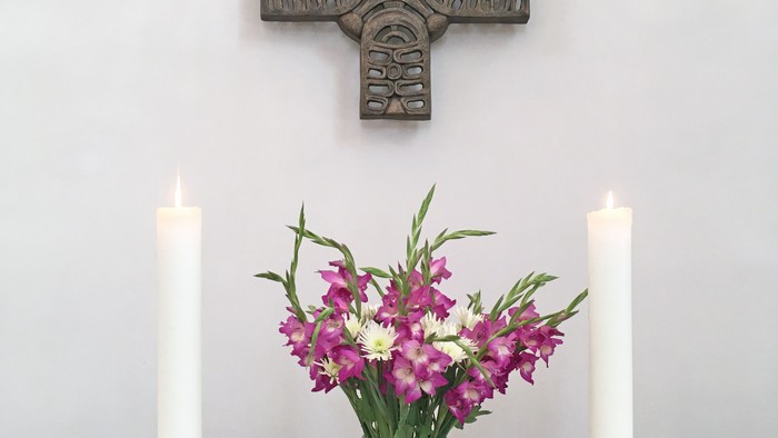 Ein Kreuz, zwei Kerzen, eine Vase mit Blumen und eine offene Bibel auf einem Tisch
