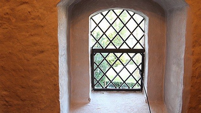 Et lille buet vindue med diamantmønstrede jernstænger indsat i en rustik, struktureret mur.