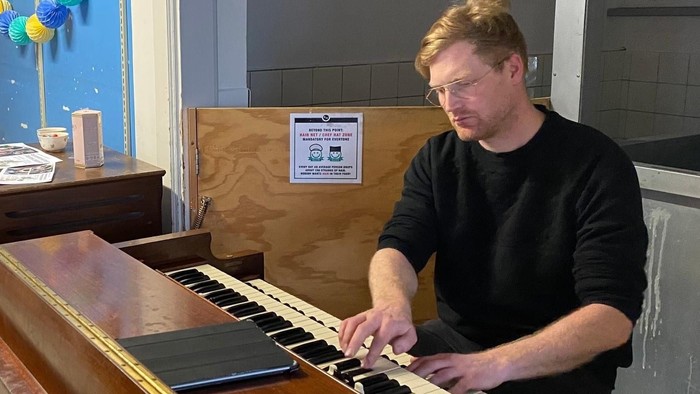 En mand spiller piano i et rum med blå vegne og farverige dekorationer.