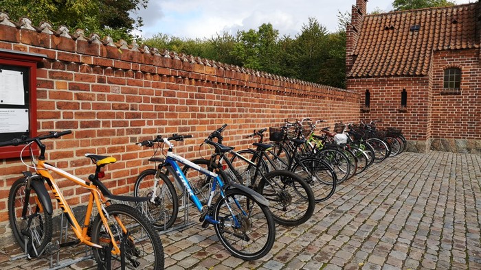 En rekke cykler parkeret ved murstengevær og røde hus.