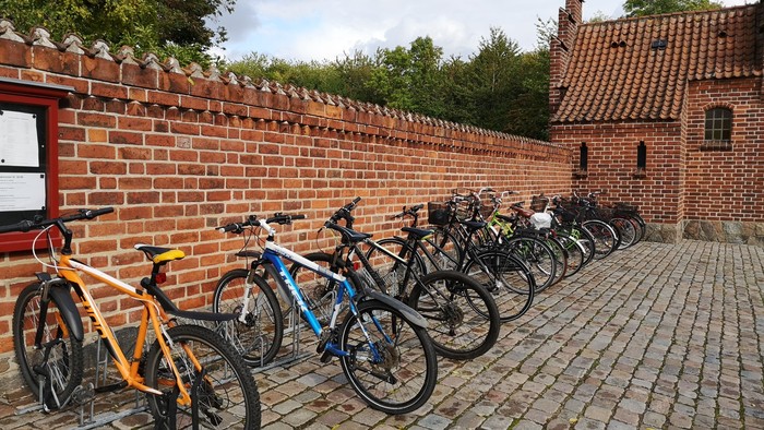 En rekke cykler parkeret ved murstengevær og røde hus.