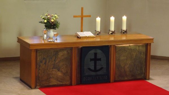 Ein hölzerner Altar mit Kreuz, Kerzen und Blumen in einem Raum