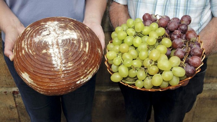 Zwei Personen halten ein Tablett mit Brot und einen Korb mit Trauben.
