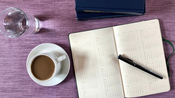 En skriveblok, en kaffe, en pen og en bog på en bord.