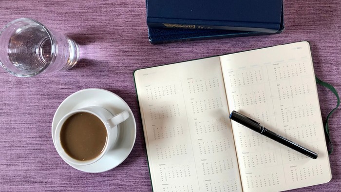 En skriveblok, en kaffe, en pen og en bog på en bord.