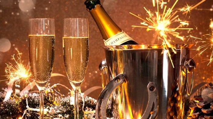 En festlig scene med champagneglas, flaske og isterninger, dekoreret med lys og pynt.