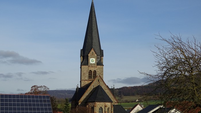 Kirchturm mit Uhr und Wetterfahne vor blauem Himmel