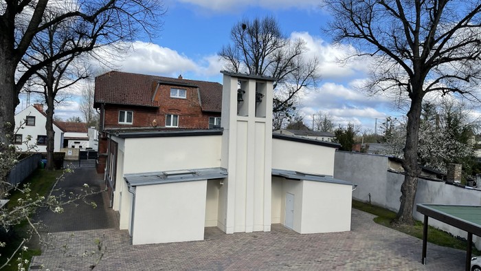 Modernes weißes Gebäude mit einzigartiger Architektur, umgeben von Bäumen und anderen Häusern.