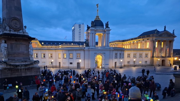 Menschen versammeln sich auf einem Platz und halten Laternen während einer Abendveranstaltung in der Nähe historischer Architektur.