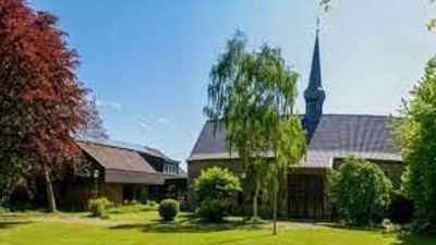 Ein Kirchengebäude mit hohem Turm und grünem Dach, umgeben von Bäumen und Rasen.