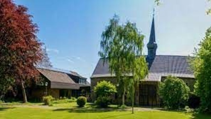 Ein Kirchengebäude mit hohem Turm und grünem Dach, umgeben von Bäumen und Rasen.