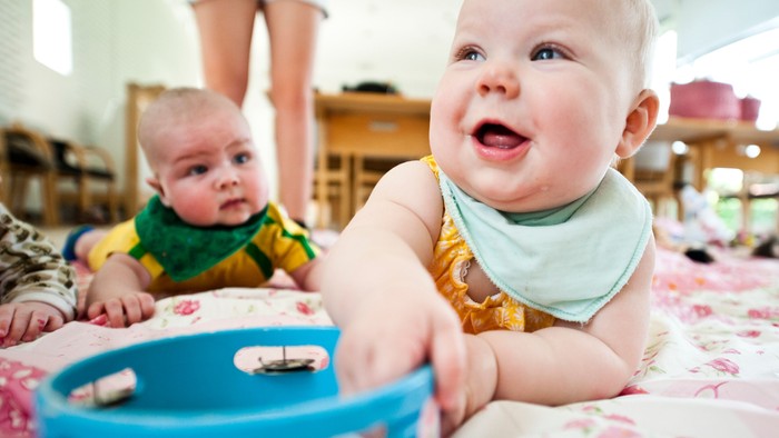 To børn ligger på en matras og lejer med en blå bæger.