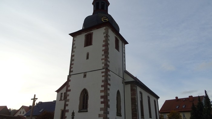 Weiße Kirche mit roter Umrandung und hohem Turm auf Friedhof