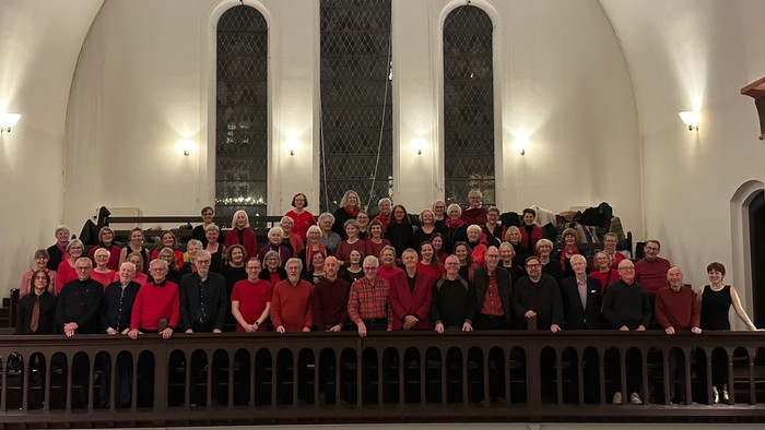 En stor gruppe af korister poserer på et scenetårn i en kirke.