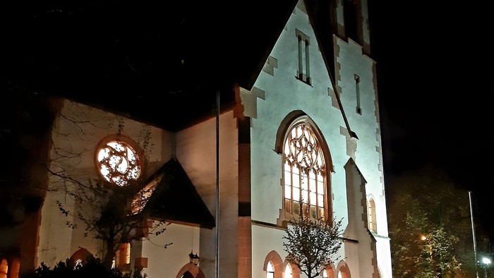 Kirchengrundstück bei Nacht mit beleuchteten Fenstern und Uhr